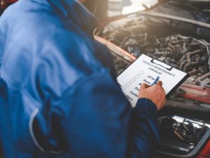 Mechanic checking vehicle maintenance checklist near Hyundai engine, diagnosing potential engine failure issues.