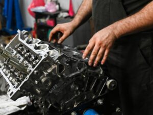 Mechanic working on reconditioned engine parts, disassembling a Kia engine block in a workshop.