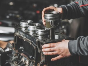 A mechanic inspecting an engine with excessive oil consumption, likely caused by worn piston rings or cylinder walls.